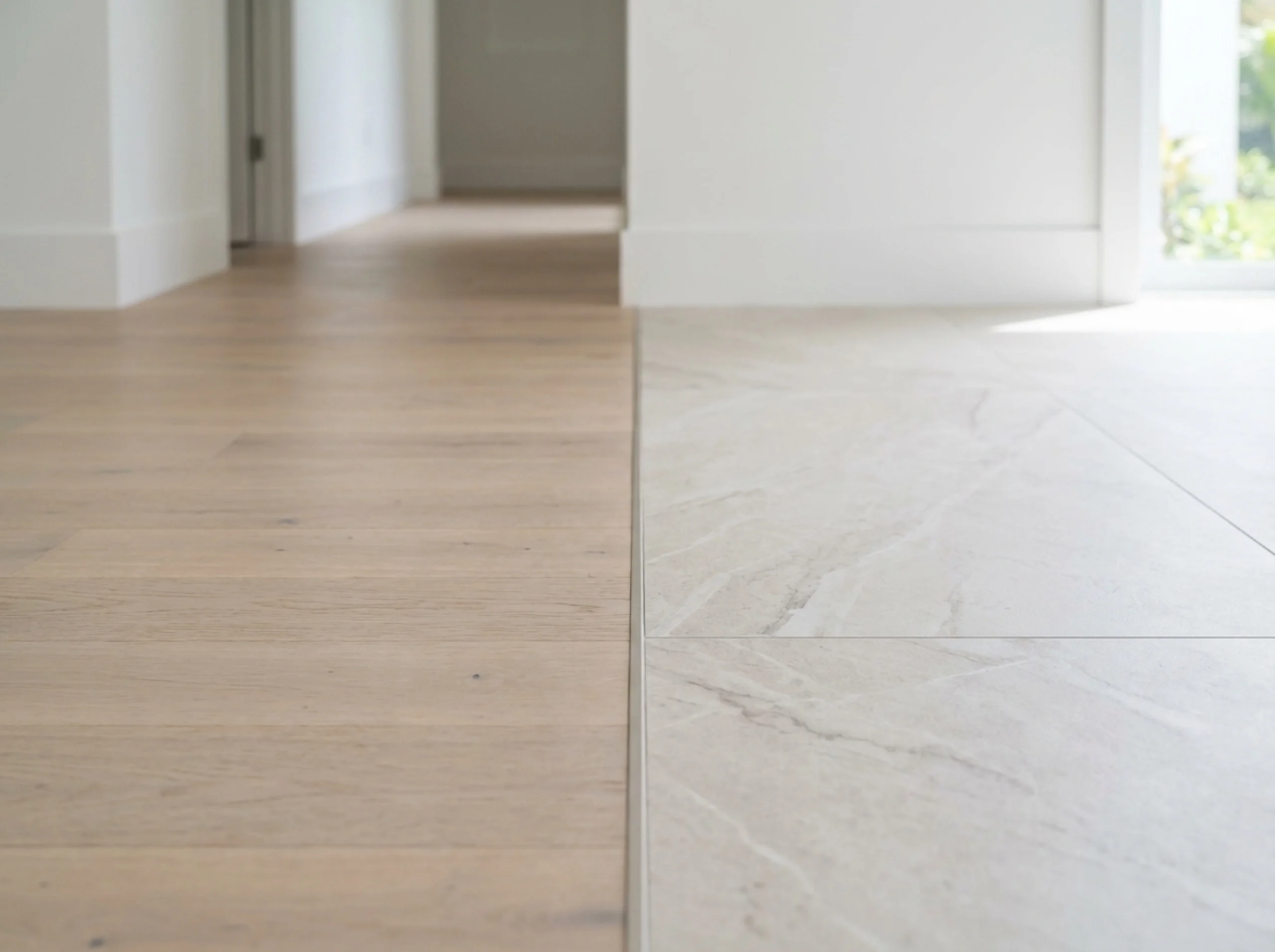 Flush transition strip between engineered white oak and large-format tile in a hallway